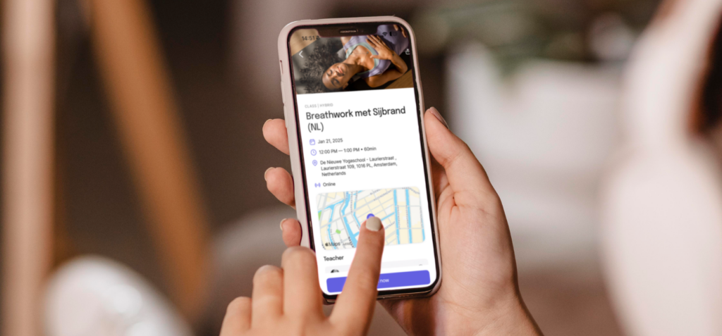 handen die een telefoon vasthouden met daarop een afbeelding van de app van de nieuwe yogaschool