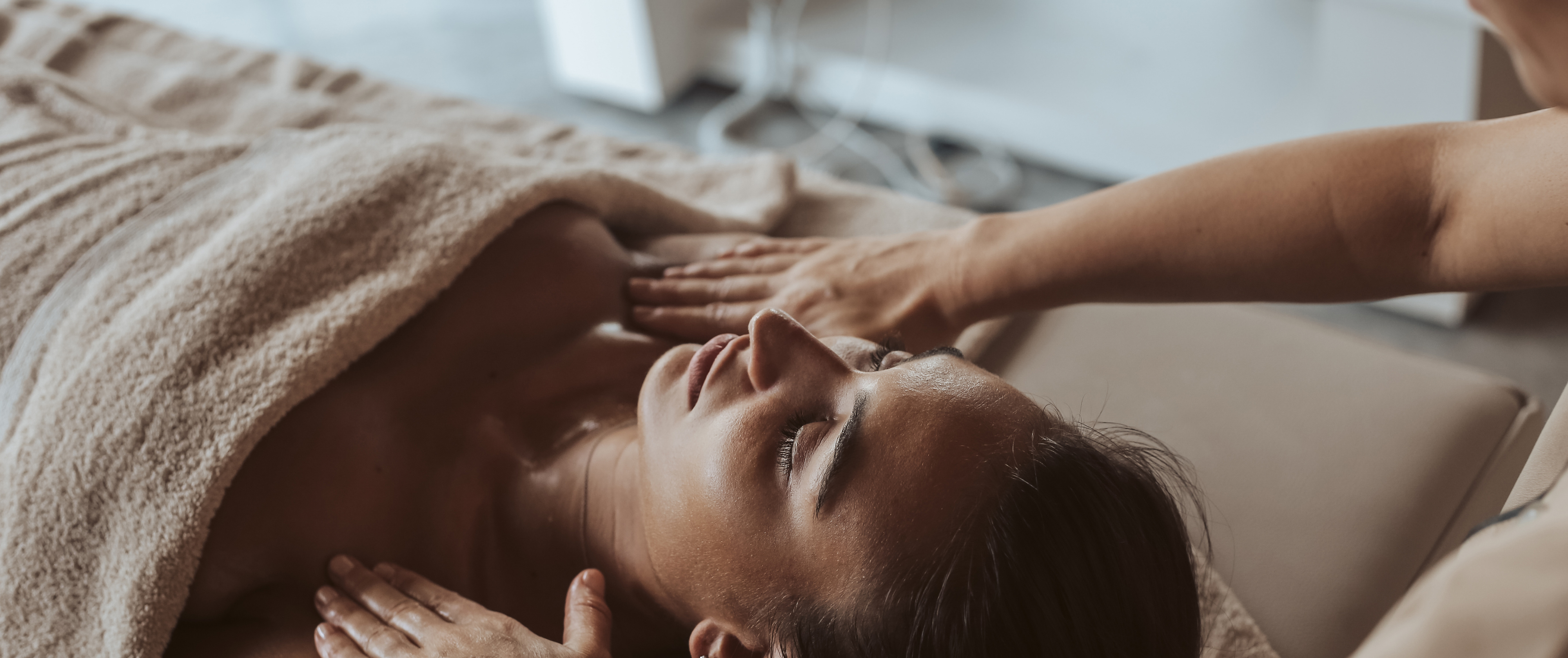 Vrouw ligt op de behandeltafel met behandelaars handen die zacht op haar rusten.