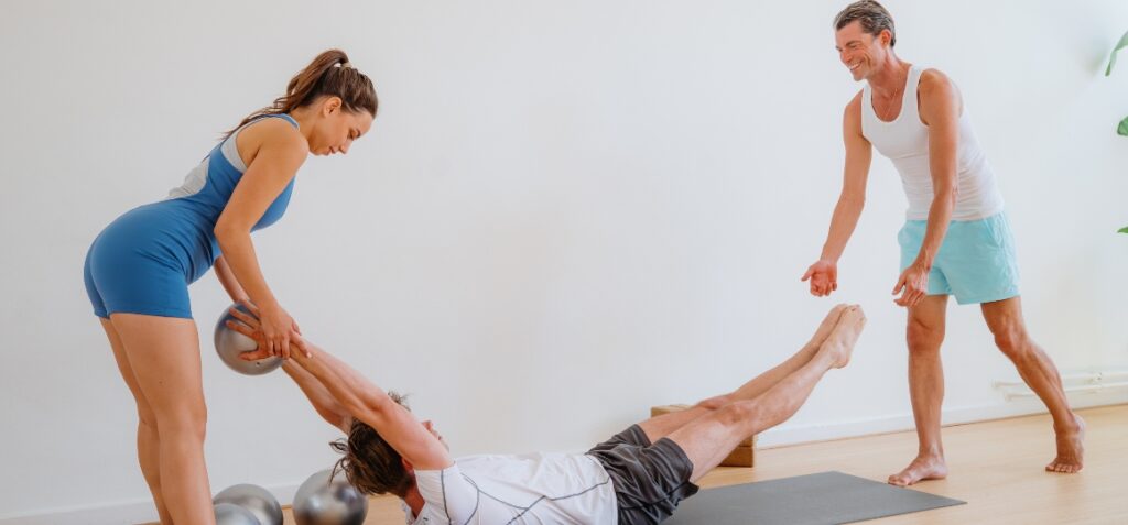 two students and teacher practicing pilates pose during pilates training