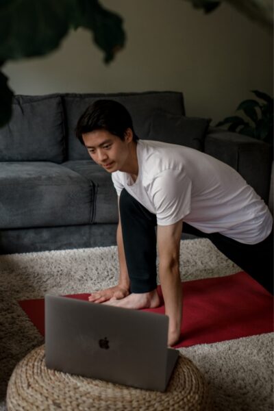 persoon die thuis yoga beoefent met een laptop met livestreamles
