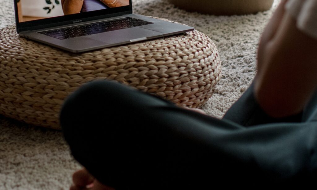 persoon die thuis yoga beoefent met een livestream les op de laptop