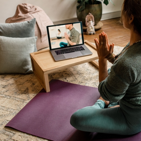 Student voor een laptop die thuis een online yogales van De Nieuwe Yogaschool volgt