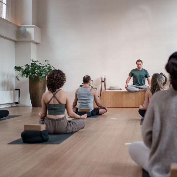 Leraar die lesgeeft aan groep yogastudenten in de ruime, lichte studio 1 van De Nieuwe Yogaschool